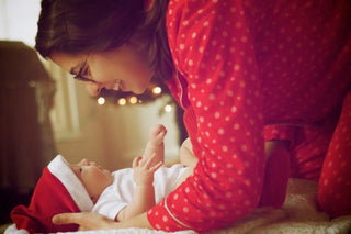 Baby wearing white clothing lying down while reaching upward.