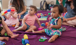 Young children sitting on purple mats during playtime with colorful toys scattered around them.