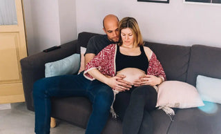 A couple sitting together on a grey couch during pregnancy.