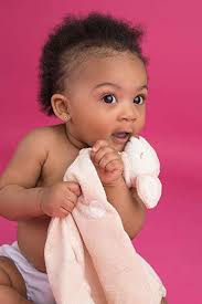 A baby holding a soft white blanket against a pink backdrop.