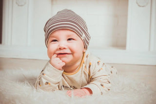 A smiling baby wearing a striped beanie and cream-colored outfit.