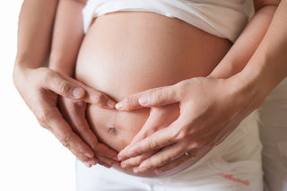 Hands forming a heart shape over a pregnant belly.